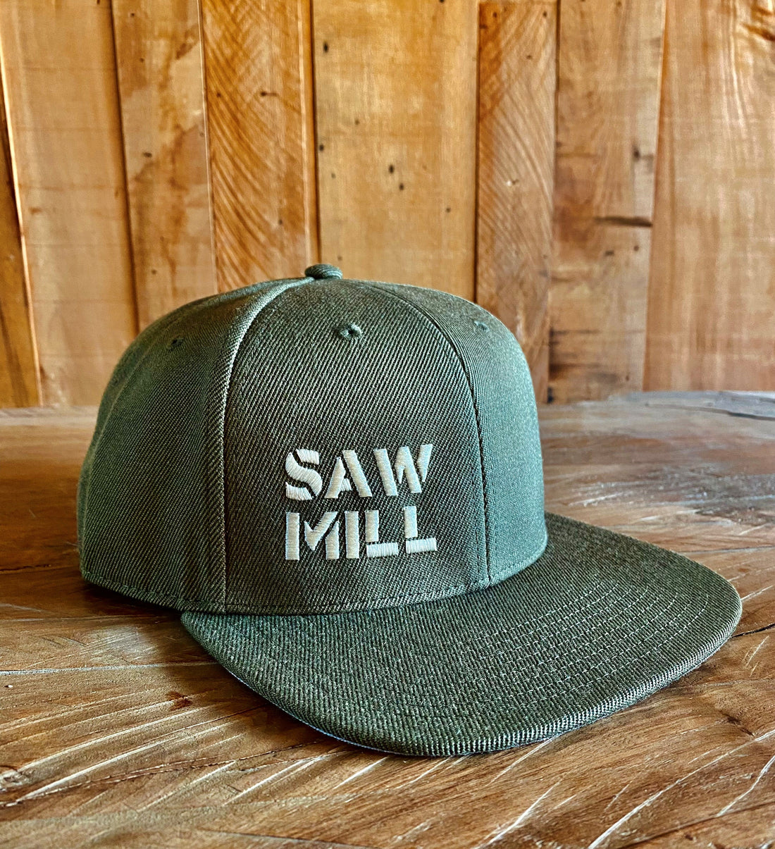 Green cap with 'Saw Mill' text on a wooden surface and background
